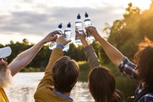 Four,Friends,Cheering,With,Water,Bottles,Standing,On,The,Beach